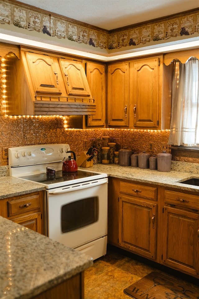 kitchen with white electric range, tasteful backsplash, brown cabinetry, and light stone counters