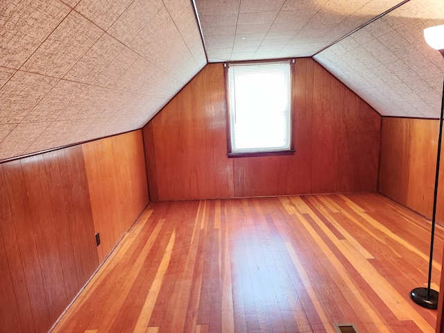 additional living space with light hardwood / wood-style flooring, lofted ceiling, and wood walls