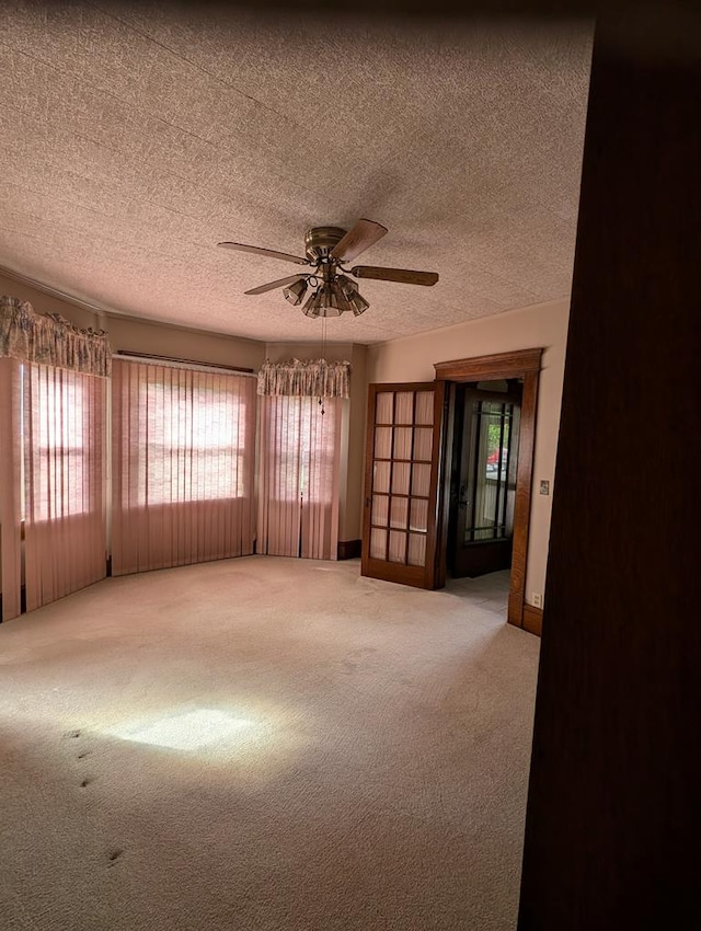 empty room featuring a textured ceiling, light colored carpet, and ceiling fan