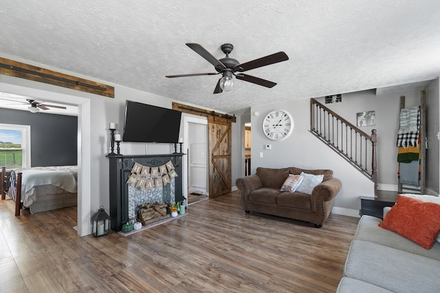 living room with a barn door, ceiling fan, dark hardwood / wood-style flooring, and a textured ceiling