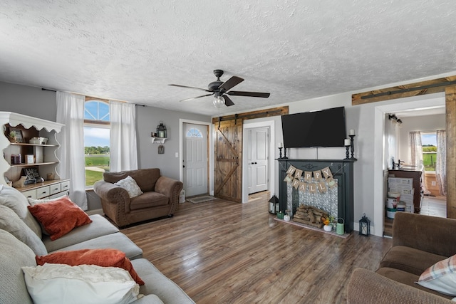 living room with dark hardwood / wood-style floors, a barn door, ceiling fan, a textured ceiling, and a fireplace