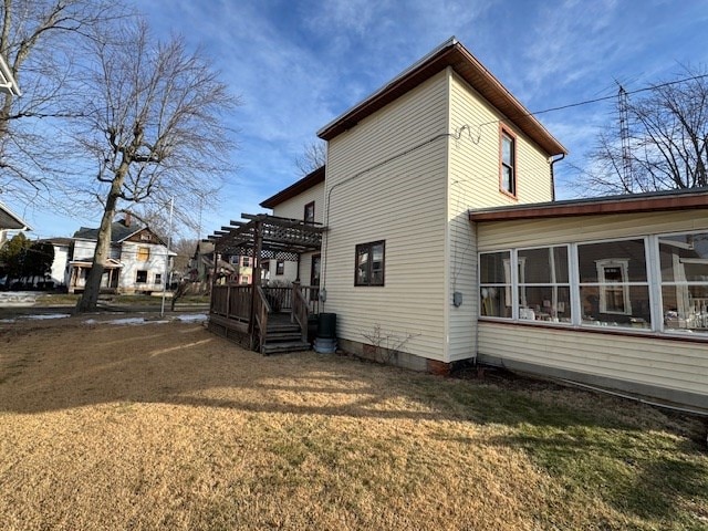 view of side of home with a wooden deck, a sunroom, a pergola, and a lawn