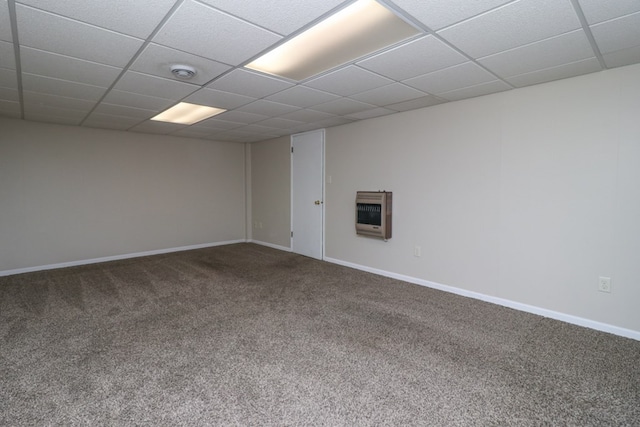 empty room with heating unit, baseboards, carpet floors, and a drop ceiling