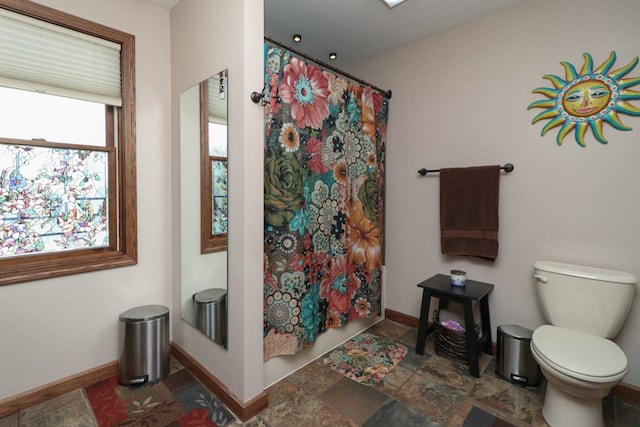 bathroom with toilet, stone finish flooring, and baseboards