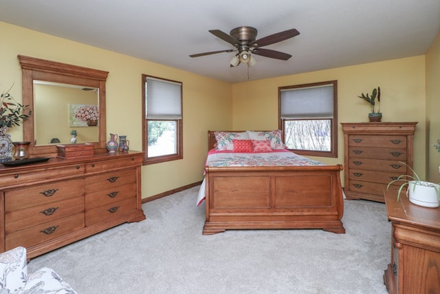 bedroom with a ceiling fan, light carpet, baseboards, and multiple windows