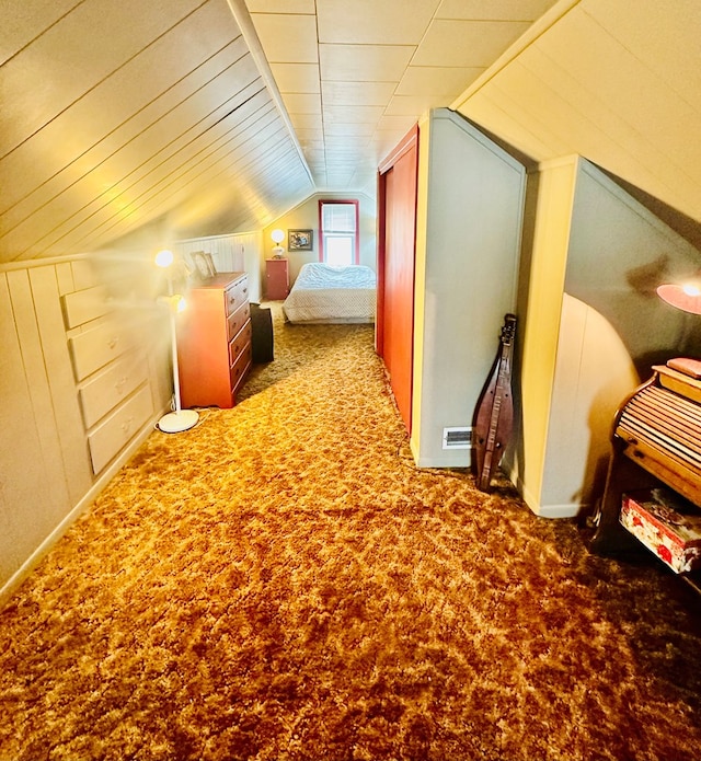 unfurnished bedroom with carpet flooring, wooden walls, and vaulted ceiling