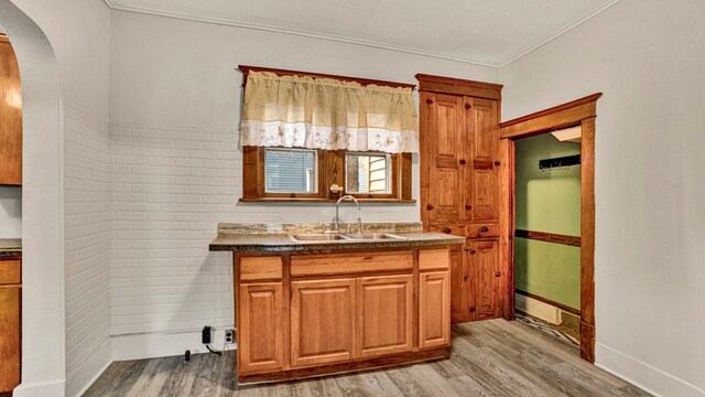 kitchen featuring sink, ornamental molding, brick wall, and light wood-type flooring