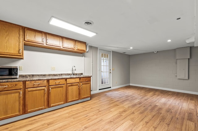 kitchen featuring brown cabinetry, stainless steel microwave, and light wood-style flooring