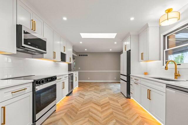 kitchen with stainless steel appliances, beverage cooler, a sink, a skylight, and decorative backsplash