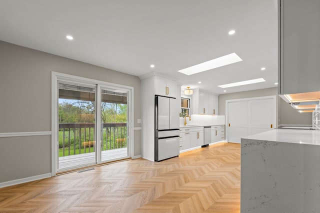 kitchen featuring fridge, dishwasher, a skylight, white cabinets, and a sink