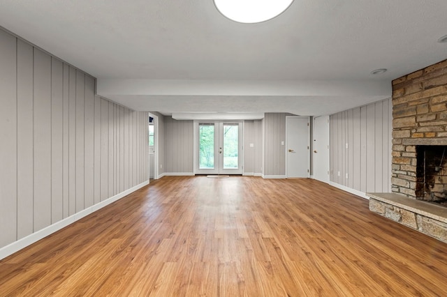unfurnished living room with light wood finished floors, a stone fireplace, baseboards, and wooden walls