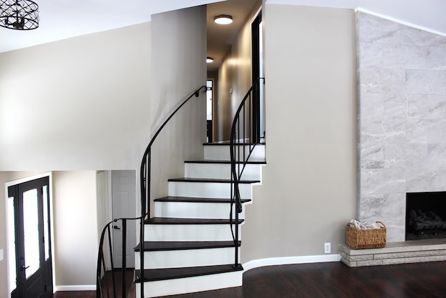 stairway featuring baseboards, a high ceiling, a fireplace, and wood finished floors