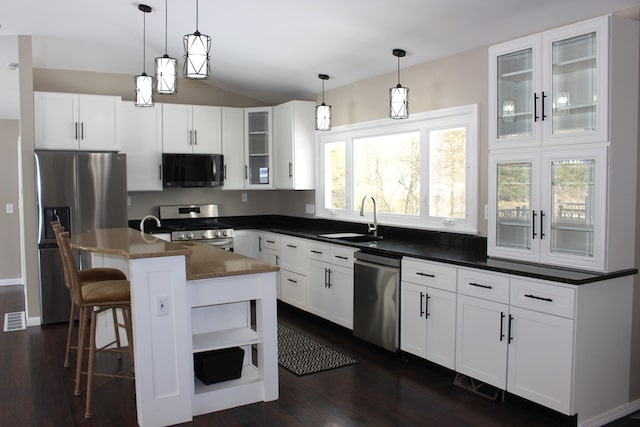 kitchen featuring appliances with stainless steel finishes, dark countertops, dark wood finished floors, a sink, and glass insert cabinets