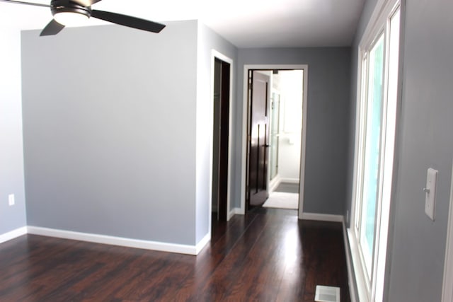 empty room featuring a ceiling fan, baseboards, visible vents, and dark wood-type flooring