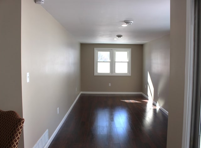 spare room with baseboards, visible vents, and dark wood-type flooring