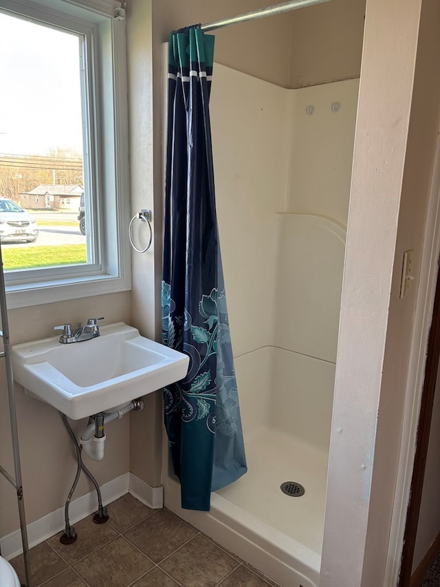 bathroom featuring baseboards, tile patterned flooring, a sink, and a stall shower