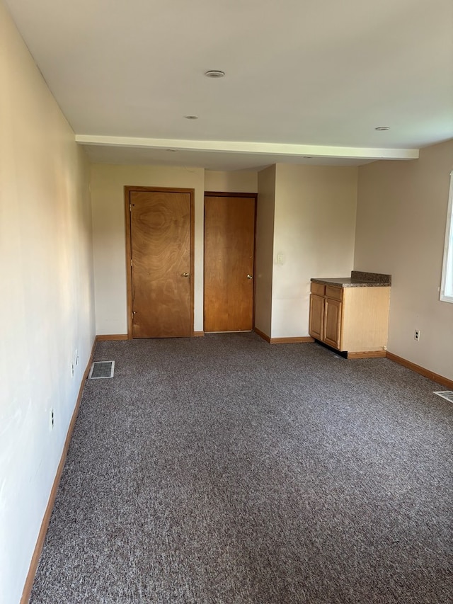 empty room with dark colored carpet, visible vents, and baseboards