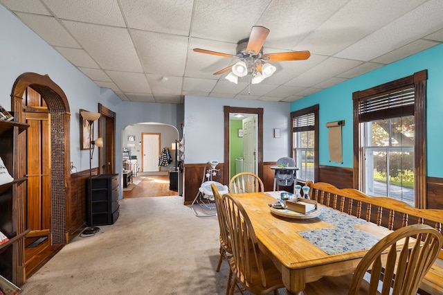 carpeted dining space featuring a paneled ceiling, ceiling fan, and wooden walls