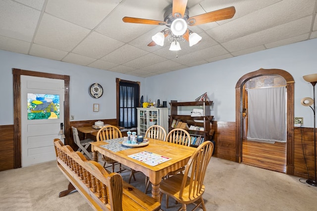 carpeted dining area featuring a paneled ceiling, wood walls, and ceiling fan