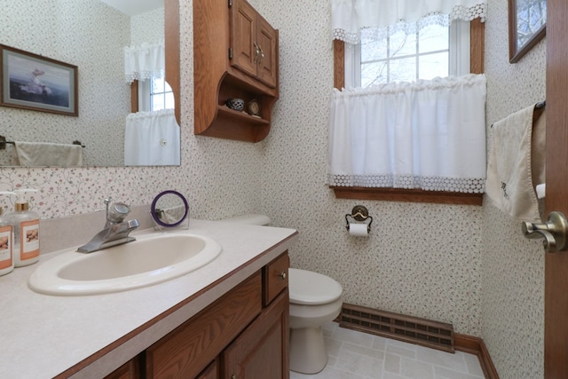 bathroom with toilet, a healthy amount of sunlight, and wallpapered walls