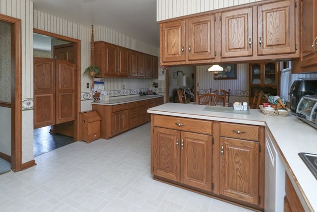 kitchen featuring brown cabinets, a peninsula, wallpapered walls, and light countertops