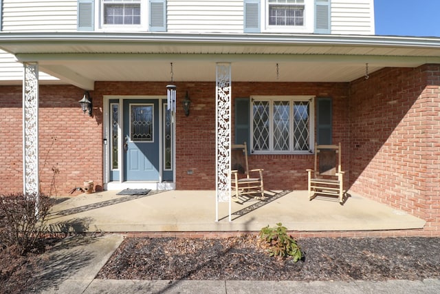entrance to property featuring a porch and brick siding