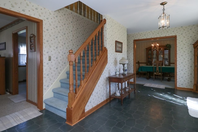 stairs featuring baseboards, stone finish floor, an inviting chandelier, and wallpapered walls
