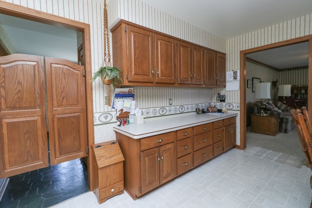 kitchen featuring brown cabinetry, light countertops, and wallpapered walls