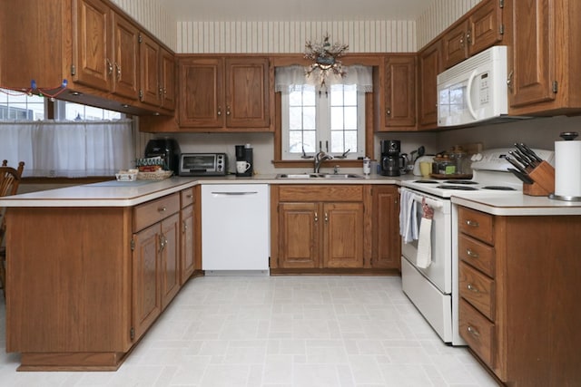 kitchen with white appliances, wallpapered walls, a peninsula, and a sink