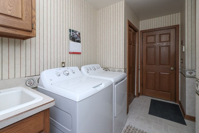 clothes washing area with a sink, cabinet space, independent washer and dryer, and wallpapered walls