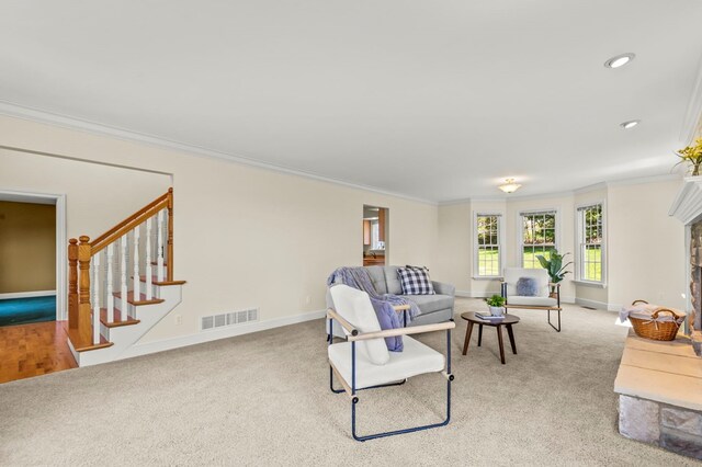 carpeted living area with baseboards, visible vents, a fireplace with raised hearth, stairs, and crown molding