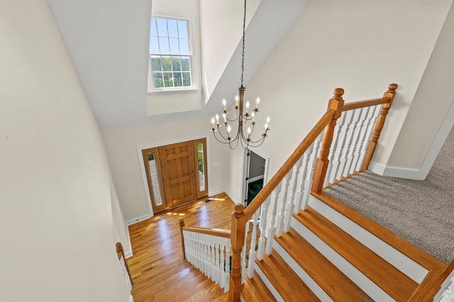 foyer entrance featuring stairs, wood finished floors, a chandelier, baseboards, and a high ceiling