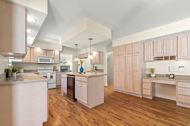 kitchen with a sink, hanging light fixtures, light wood-style floors, white appliances, and wine cooler