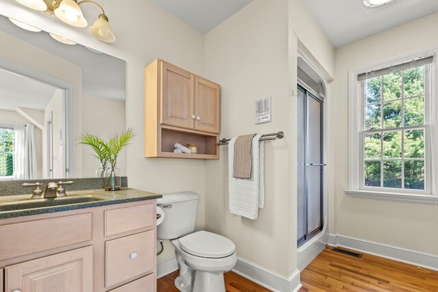 bathroom with toilet, wood finished floors, a shower with shower door, baseboards, and visible vents