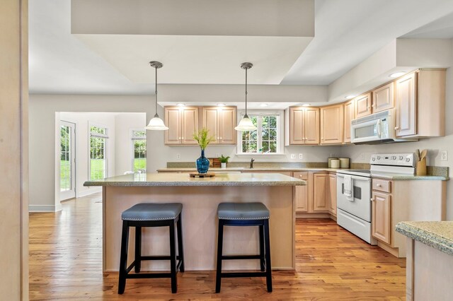 kitchen with a center island, a kitchen breakfast bar, white appliances, light brown cabinets, and light countertops