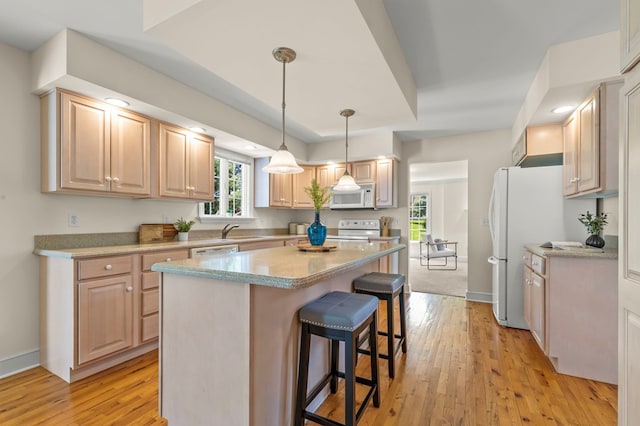 kitchen featuring a kitchen breakfast bar, light wood-style flooring, a healthy amount of sunlight, white appliances, and a kitchen island