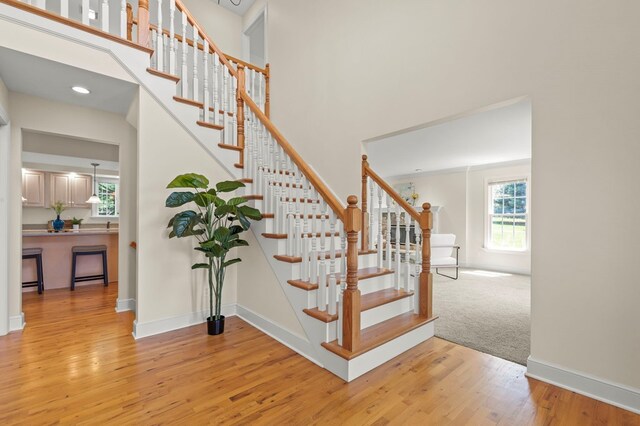 stairway with wood finished floors, a high ceiling, and baseboards