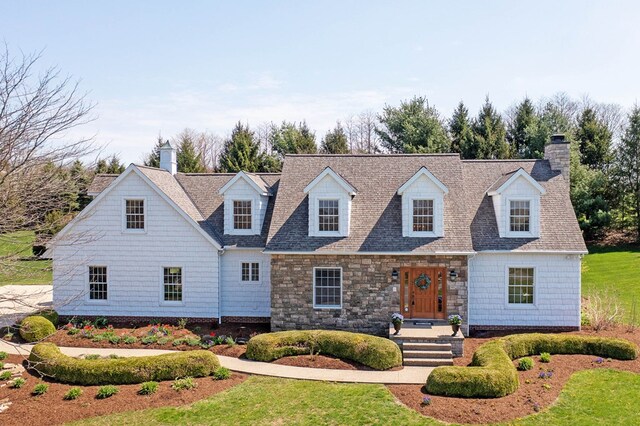 cape cod house featuring roof with shingles and a chimney
