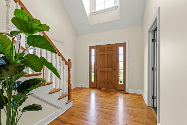 foyer entrance featuring light wood-style floors, stairway, a wealth of natural light, and high vaulted ceiling