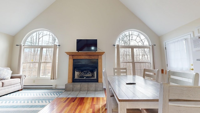 dining area with a baseboard heating unit, a healthy amount of sunlight, a fireplace, and wood finished floors