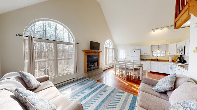 living room featuring light wood-style floors, high vaulted ceiling, baseboard heating, and a tile fireplace