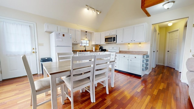 kitchen featuring high vaulted ceiling, white cabinets, freestanding refrigerator, stainless steel microwave, and wood-type flooring