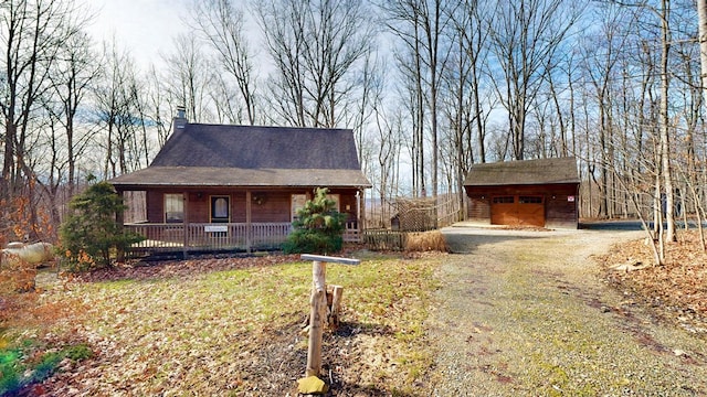 view of front of home featuring a detached garage, a chimney, covered porch, an outdoor structure, and driveway