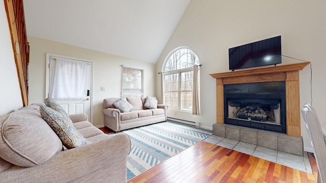 living area with hardwood / wood-style flooring, high vaulted ceiling, baseboard heating, and a tile fireplace