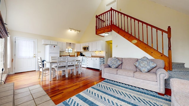 living area featuring stairs, high vaulted ceiling, track lighting, and wood finished floors