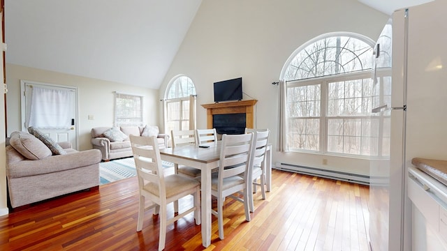 dining room with a healthy amount of sunlight, light wood-style floors, a baseboard heating unit, and high vaulted ceiling