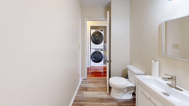 bathroom featuring toilet, wood finished floors, vanity, baseboards, and stacked washer / drying machine