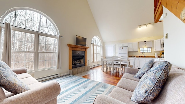 living area featuring high vaulted ceiling, light wood-type flooring, baseboard heating, and a tile fireplace