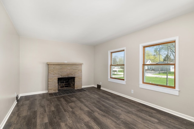 unfurnished living room featuring baseboards, a stone fireplace, and dark wood-type flooring