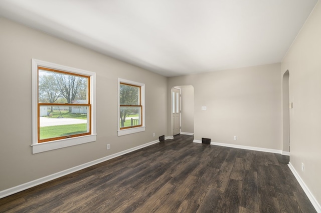 empty room with arched walkways, dark wood-style flooring, and baseboards